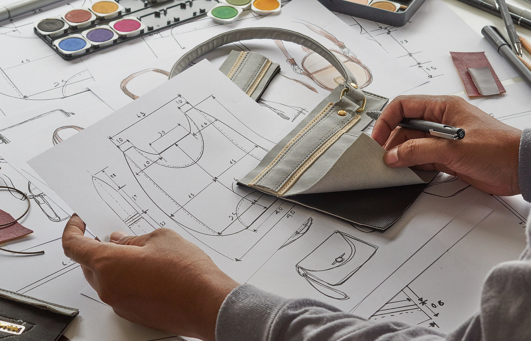 Professional leather handbag factory showing OEM custom manufacturing process with technical drawings, material samples, and skilled craftsmanship in a modern workshop